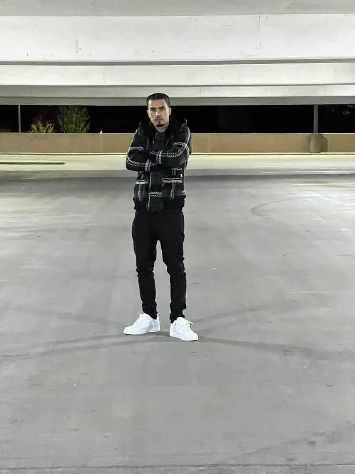 A young man standing alone in a parking garage at night.