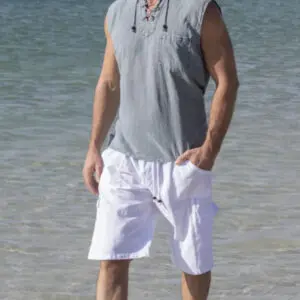 Man standing on the beach wearing a sleeveless gray shirt and white shorts.