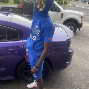 Person in blue outfit standing next to a purple car in a parking lot.
