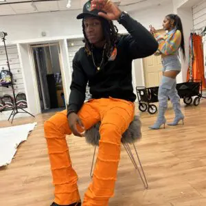 Person in bright orange pants sitting indoors, adjusting cap.