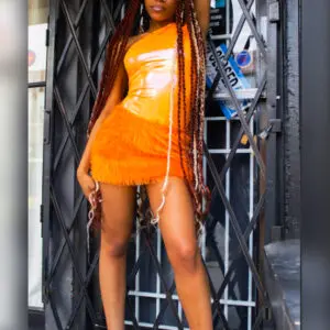 Woman in a shiny orange mini dress posing confidently indoors.