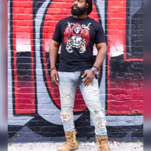 Man in ripped jeans and graphic tee standing against a graffiti wall.