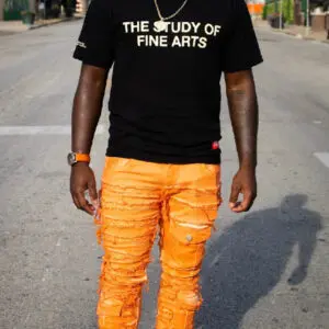 Man wearing a black T-shirt and bright orange ripped jeans walking outdoors.