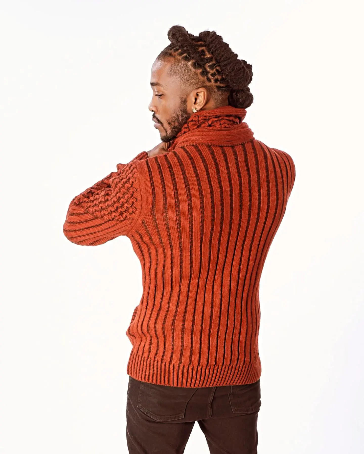 Man in a rust-colored ribbed sweater looking back.