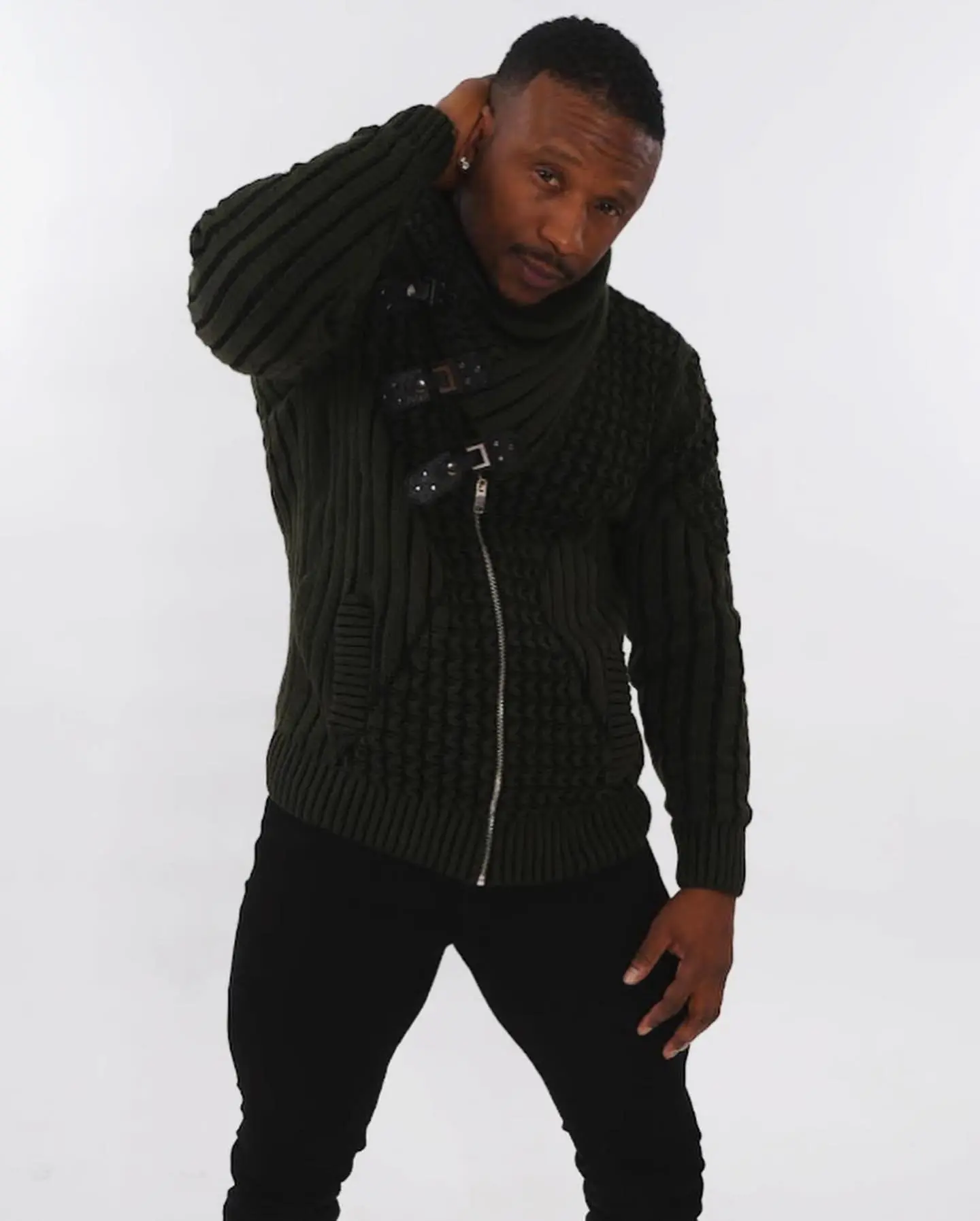Man in dark green sweater posing against a plain background.