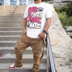A person wearing a graphic white t-shirt and brown pants stands on stairs outdoors.