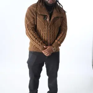 Man wearing a brown knitted sweater and black pants standing against a white background.