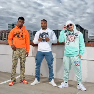 Three men posing stylishly in urban streetwear against a cloudy sky.
