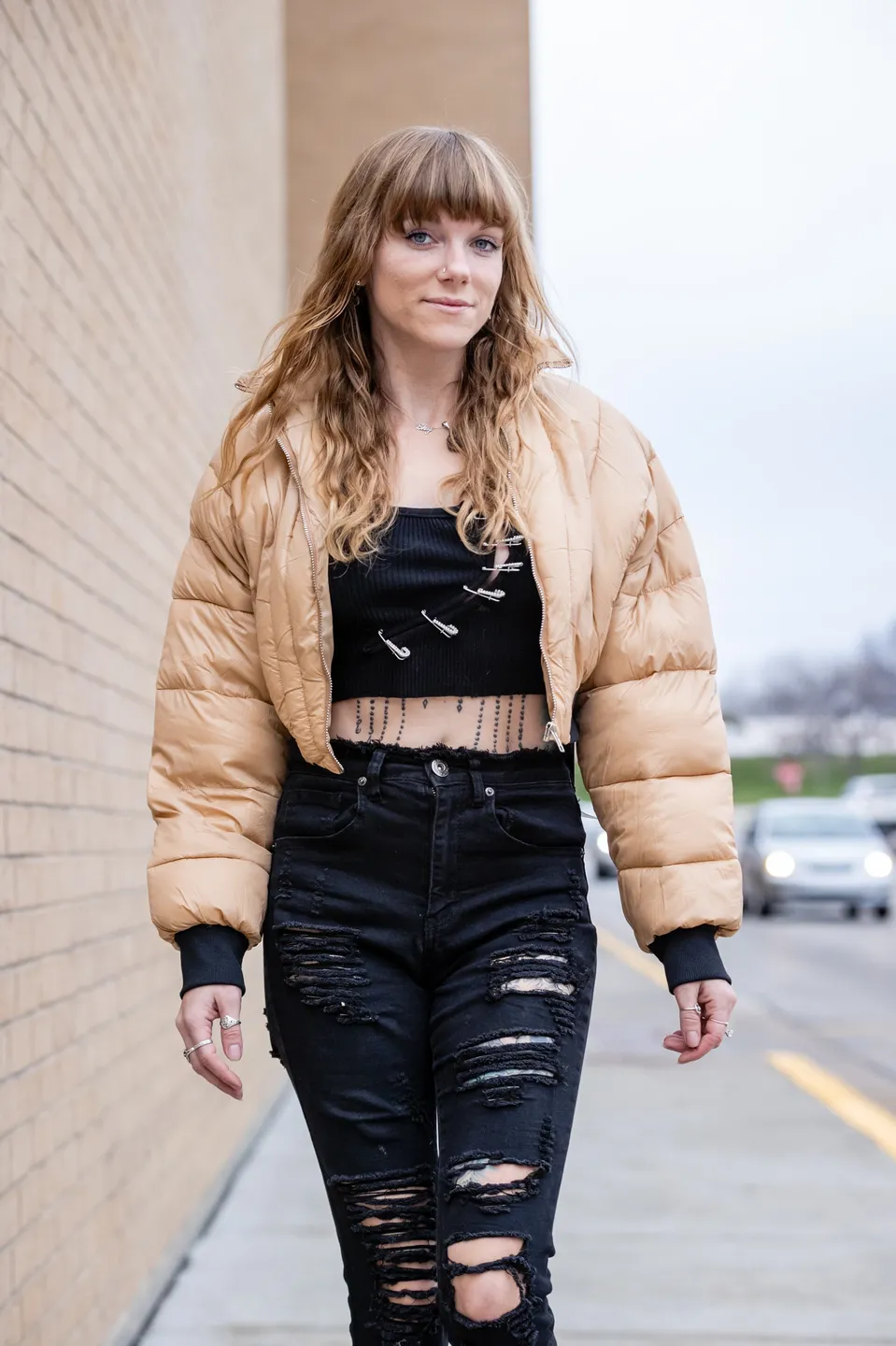 Young woman in a tan puffer jacket and ripped black jeans walking outdoors.