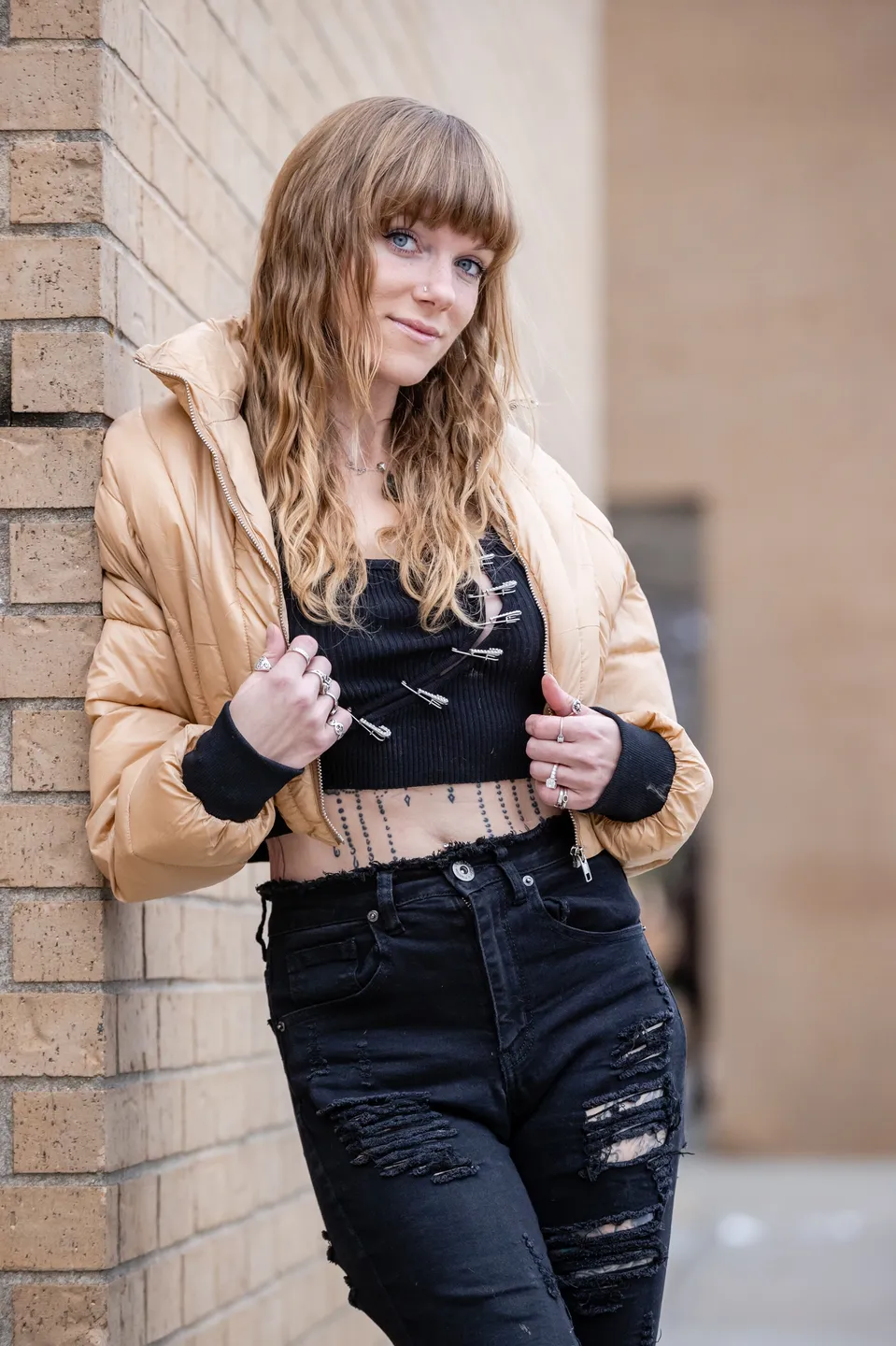 Young woman in casual outfit leaning against a brick wall.
